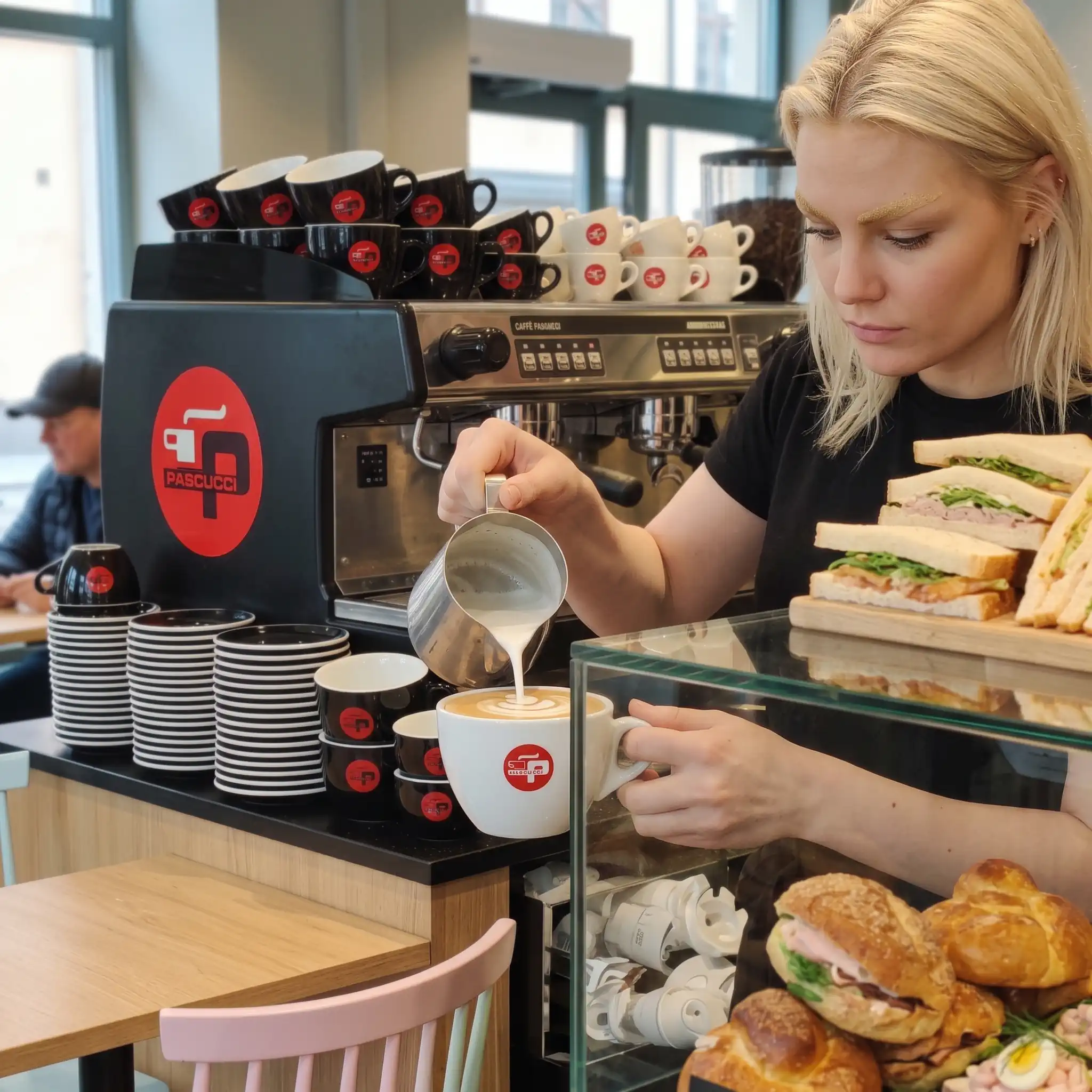 Blond kvinna gör en cappuccino i ett cafe WebP